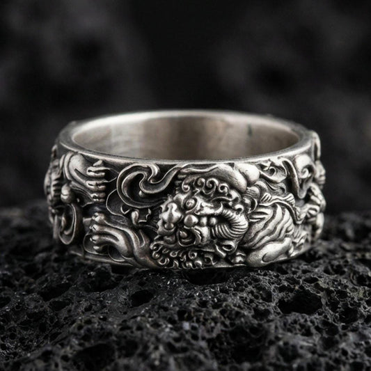 Oxidized sterling silver guardian lion band ring on volcanic stone, macro close-up highlighting deep darkened recesses, high-relief lion face, and swirling cloud details.
