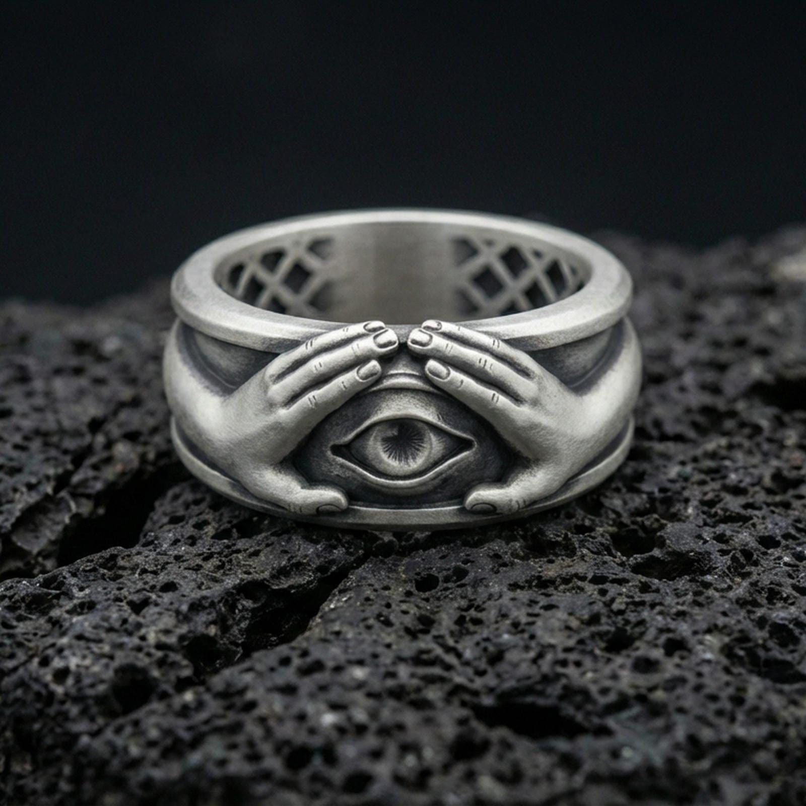Oxidized sterling silver protective eye ring on volcanic stone, macro close-up highlighting darkened recesses, sculpted hands, and sharp eye relief.