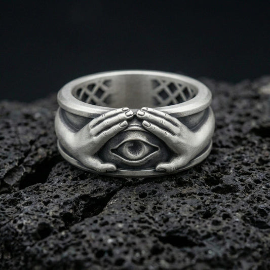 Oxidized sterling silver protective eye ring on volcanic stone, macro close-up highlighting darkened recesses, sculpted hands, and sharp eye relief.