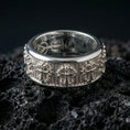 Load image into Gallery viewer, Gothic cross spinner ring on black volcanic stone, photographed in polished silver with crisp reflections along the rotating band edges.
