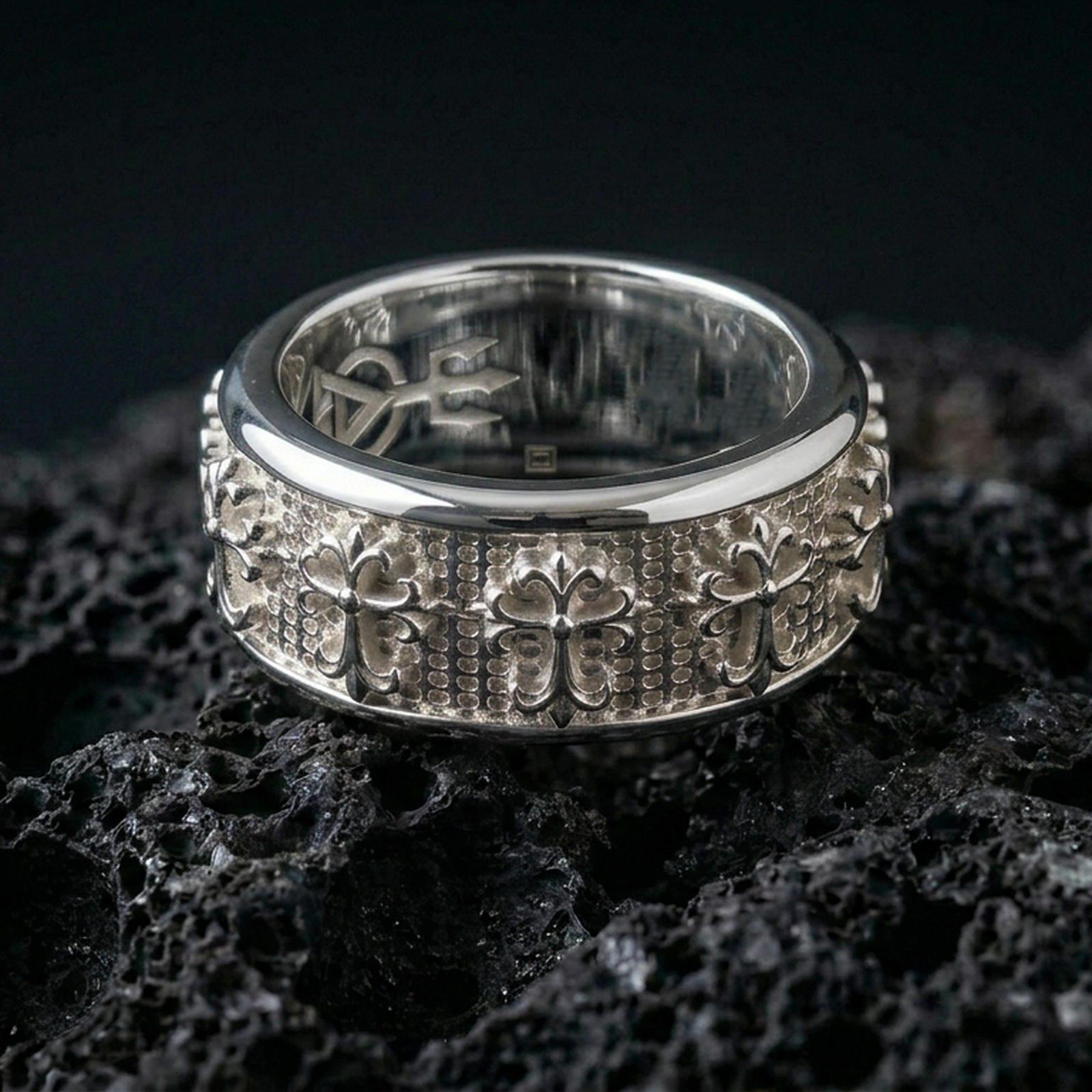 Gothic cross spinner ring on black volcanic stone, photographed in polished silver with crisp reflections along the rotating band edges.