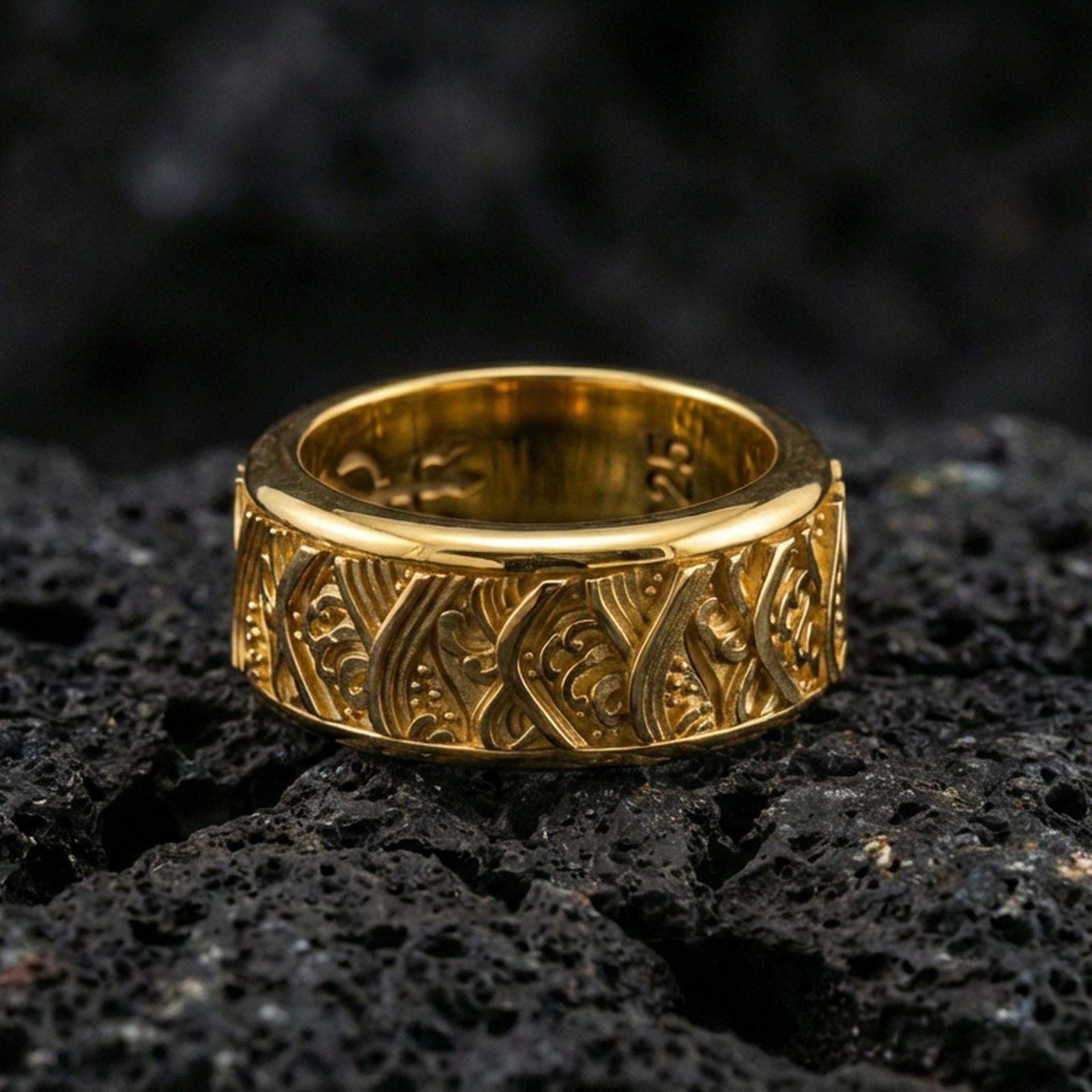 Rotating wave spinner ring on black volcanic stone, shown in a gold plated finish with warm shine accenting the ocean-wave relief across the spinner band.
