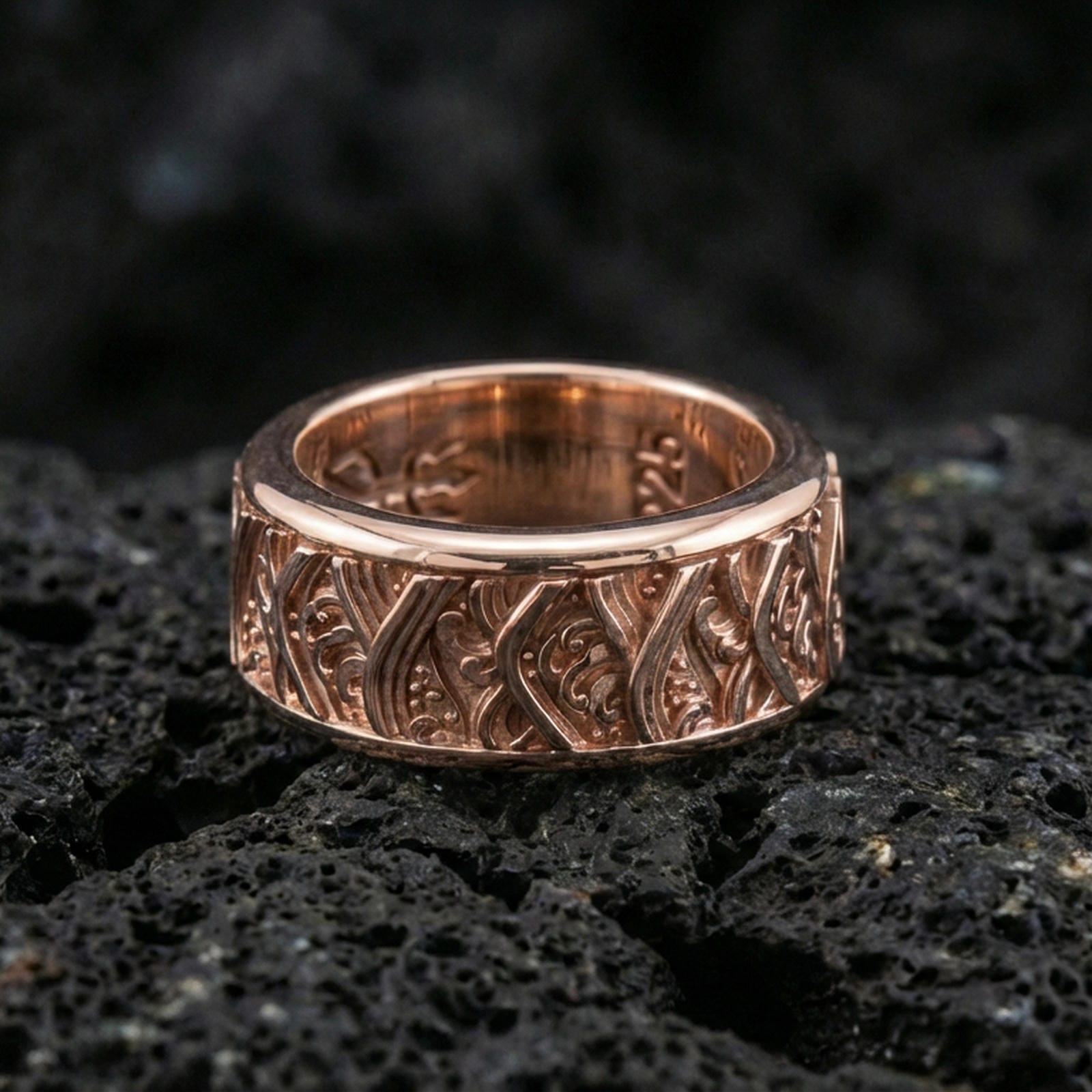 Rotating wave spinner ring on black volcanic stone, shown in a rose gold plated finish with a softer metallic glow that enhances the wave engraving depth.