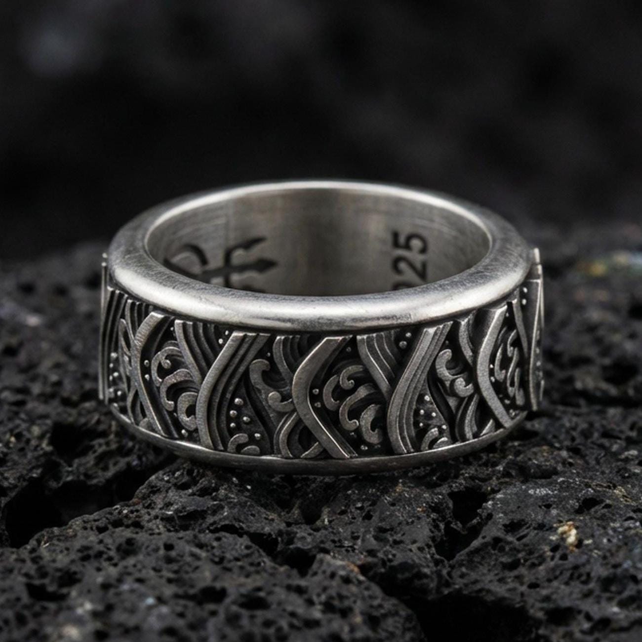 Rotating wave spinner ring on black volcanic stone, photographed in oxidized sterling silver with darkened recesses emphasizing the flowing nautical wave pattern.