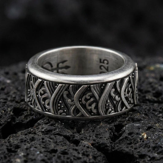Rotating wave spinner ring on black volcanic stone, photographed in oxidized sterling silver with darkened recesses emphasizing the flowing nautical wave pattern.