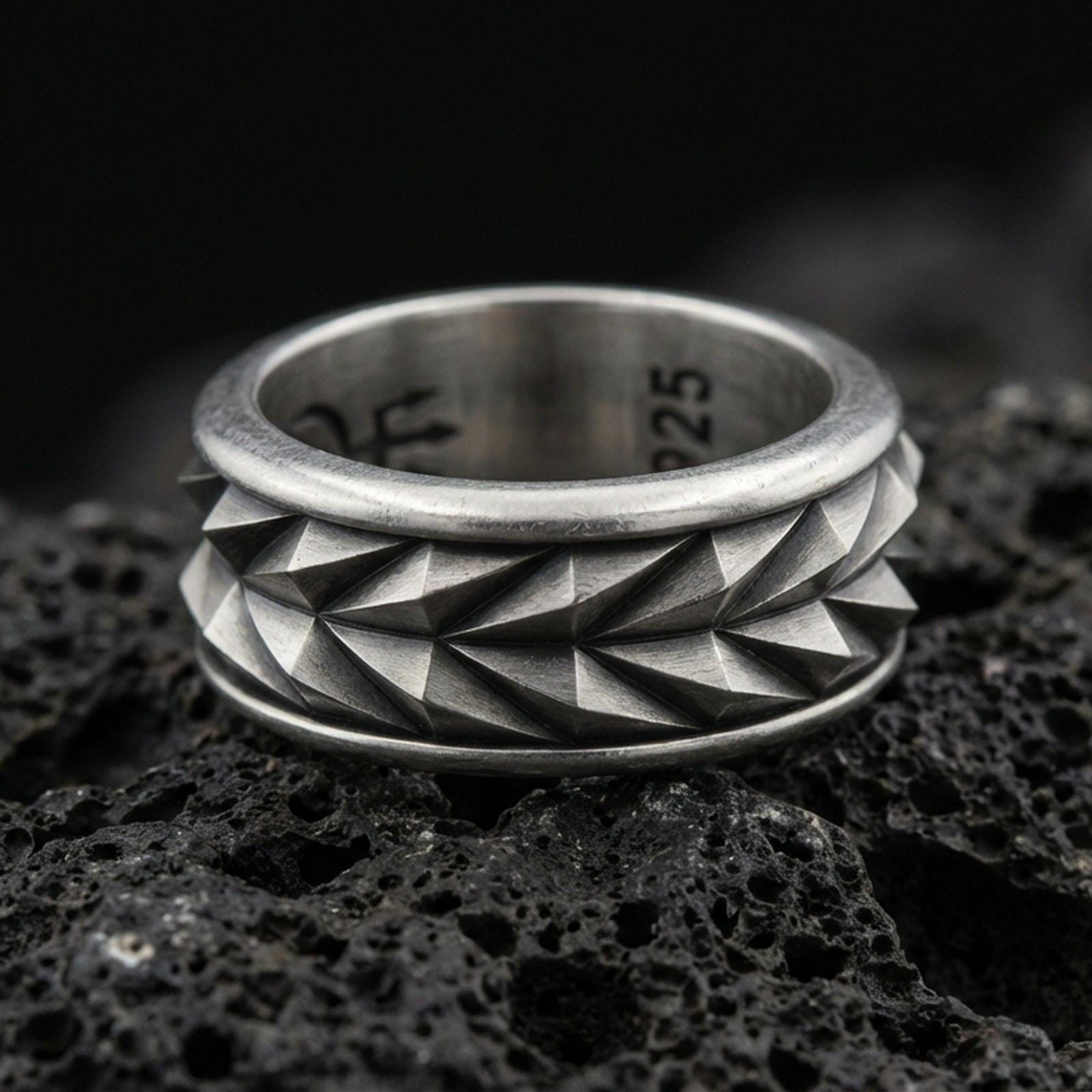 Mechanic style spinning fidget band ring on black volcanic stone, photographed in oxidized sterling silver with darkened grooves that sharpen the faceted pyramid texture.