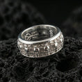 Load image into Gallery viewer, Skull motif sterling silver band ring on black volcanic stone, photographed in a polished silver look with clean highlights across the raised skull pattern.
