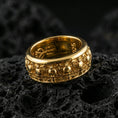Load image into Gallery viewer, Skull motif sterling silver band ring on black volcanic stone, shown in a gold plated finish that adds warm shine to the skull-and-ornament texture.
