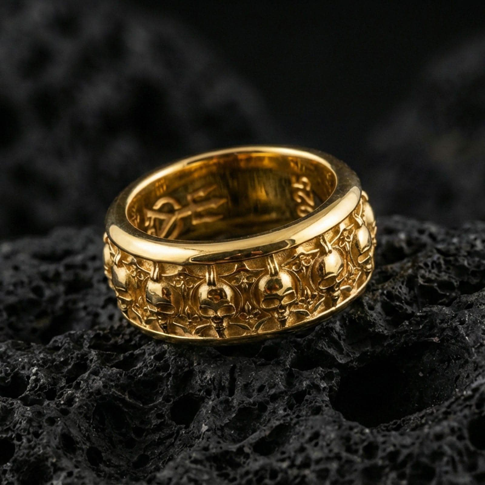 Skull motif sterling silver band ring on black volcanic stone, shown in a gold plated finish that adds warm shine to the skull-and-ornament texture.