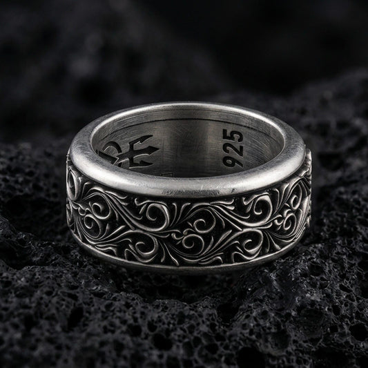 Ornate scrollwork sterling silver band ring on black volcanic stone, photographed with an oxidized finish to emphasize depth and shadow in the engraved pattern.