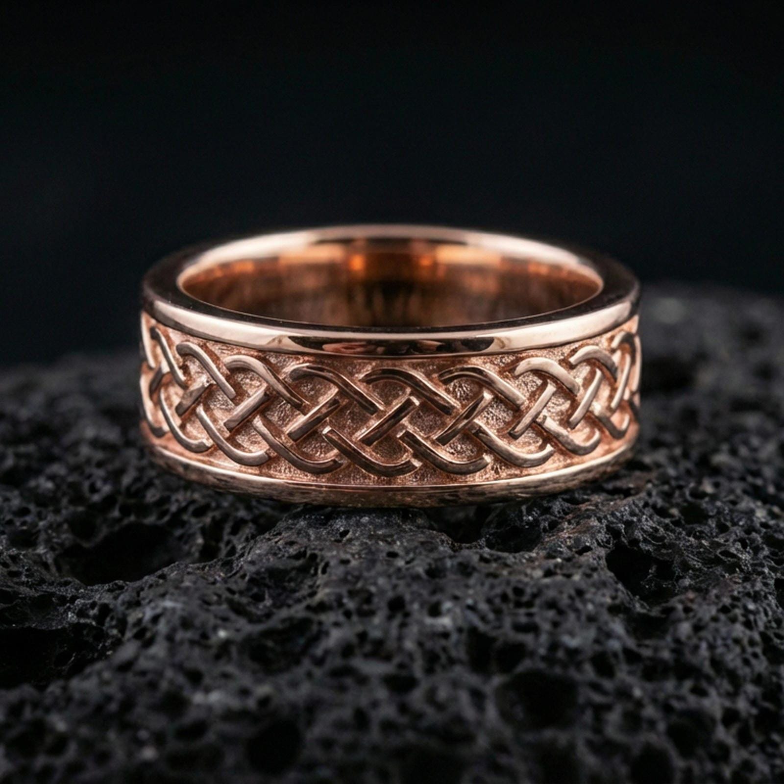 Sterling silver Celtic knot band ring on black volcanic stone, presented in a rose gold plated finish with a softer warm tone that complements the knotwork depth and borders.