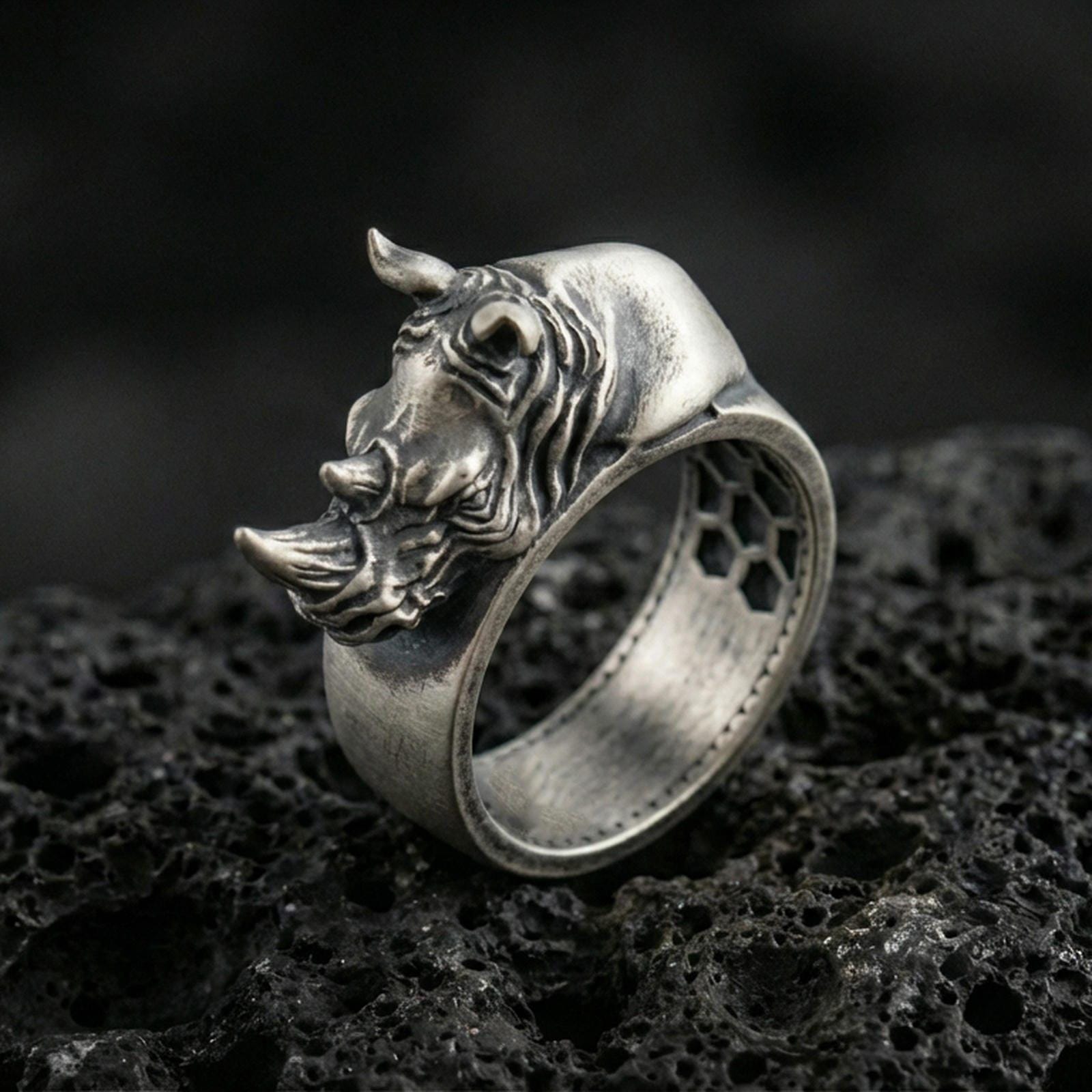 Sterling silver rhino head ring photographed on black volcanic stone, featuring an oxidized finish that deepens the shadows in the sculpted horn and facial lines.