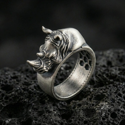 Sterling silver rhino head ring photographed on black volcanic stone, featuring an oxidized finish that deepens the shadows in the sculpted horn and facial lines.