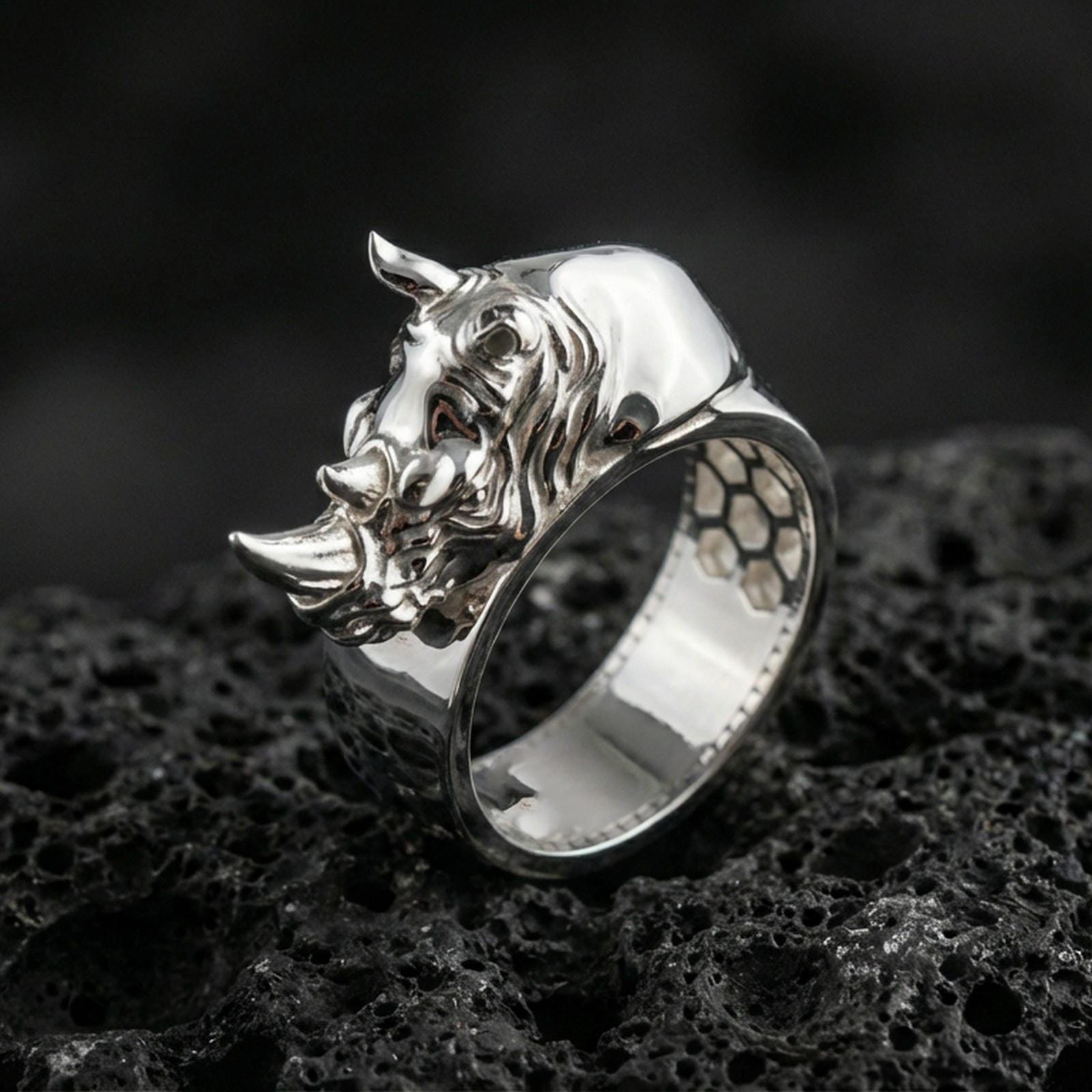 Sterling silver rhino head ring photographed on black volcanic stone, shown in a polished silver finish with clean highlights across the horn, snout, and smooth band.
