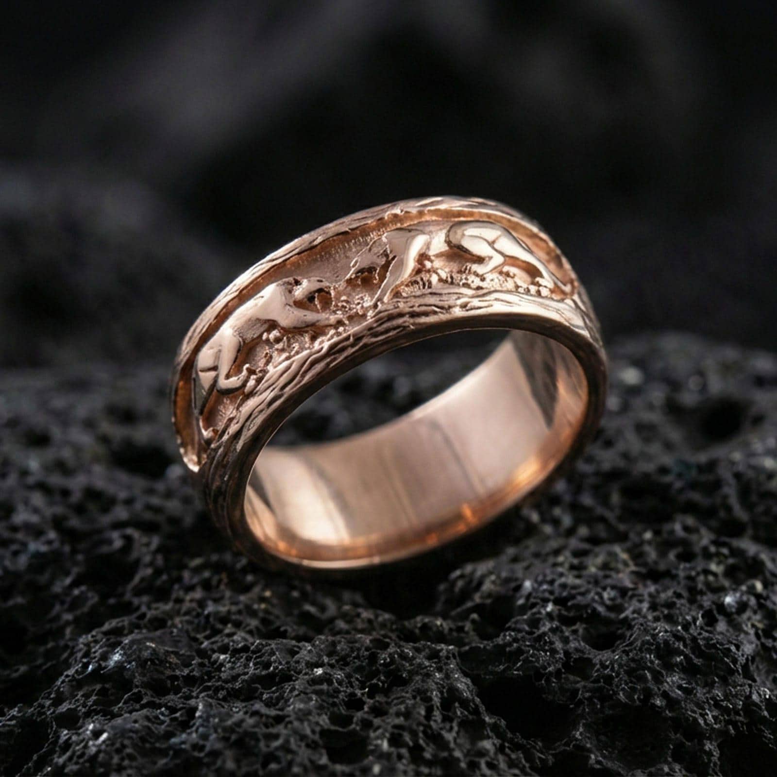 Sterling silver band ring photographed on black volcanic stone, shown in a rose gold plated finish with soft warm reflections emphasizing the engraved monkey motif.