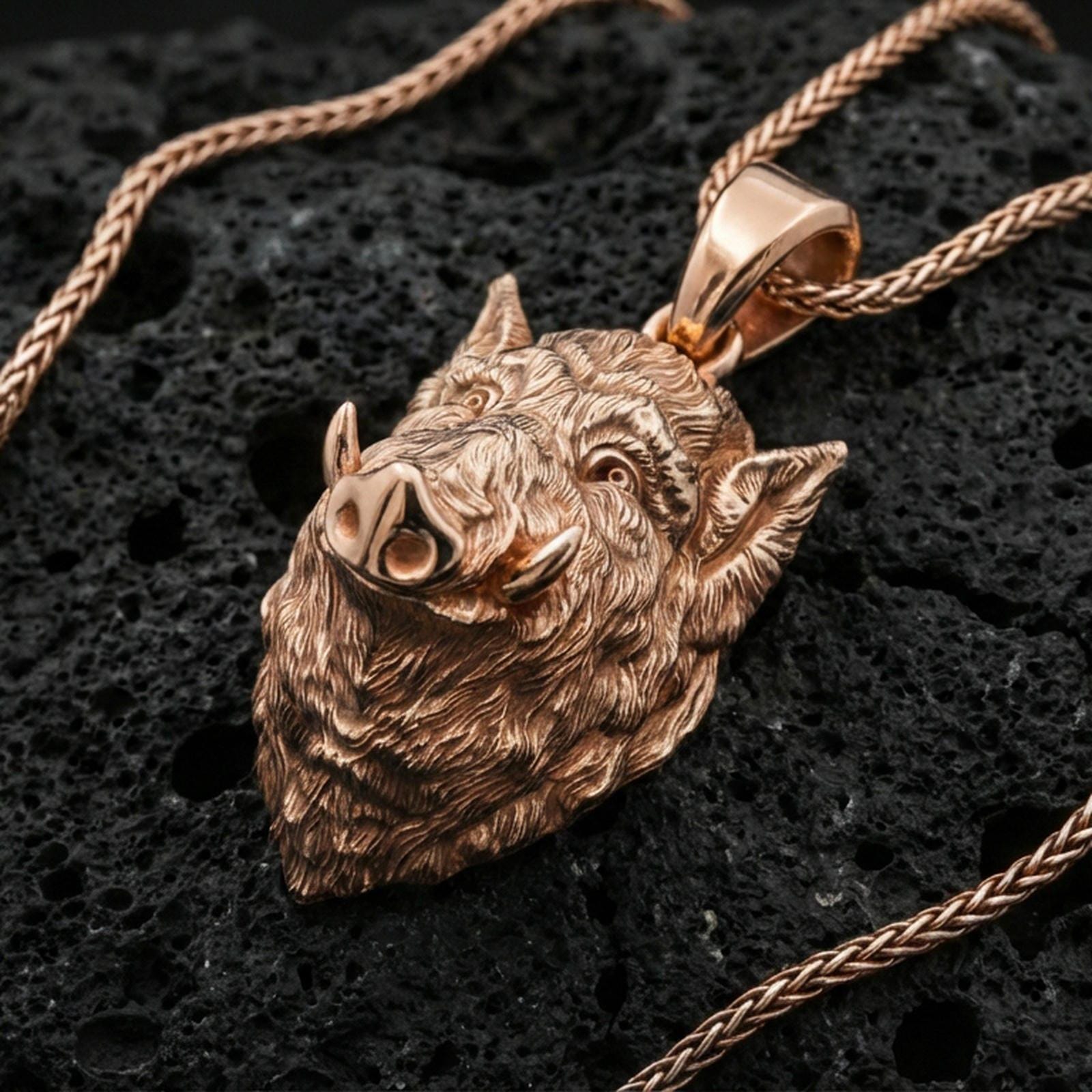 Rose gold plated boar head pendant on textured volcanic rock with braided chain, luxury close-up capturing warm tone and high-relief boar carving