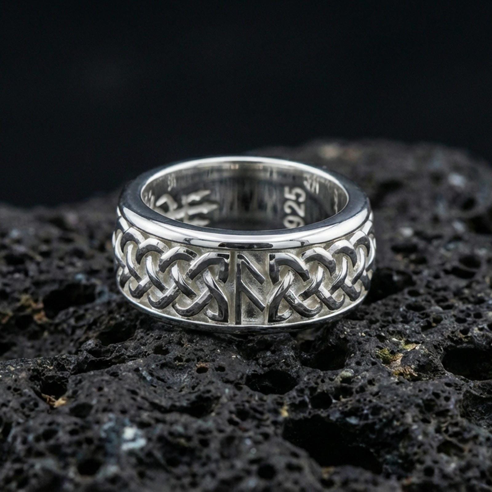 Celtic knot spinner band ring on black volcanic stone, shown in a polished silver finish with crisp reflective edges across the raised knotwork.