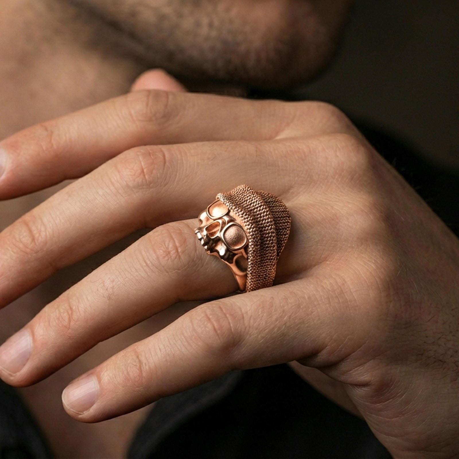 Rose gold plated skull ring with beanie and goggles on the finger, close-up lifestyle photo showcasing warm plating and edgy streetwear vibe