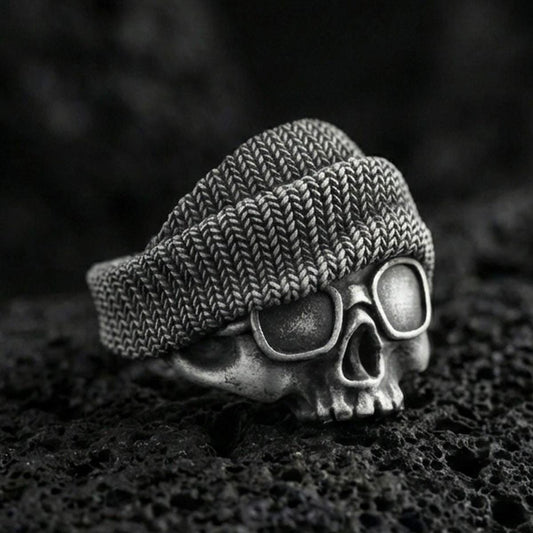 Oxidized sterling silver skull ring with beanie and goggles on black volcanic rock, macro close-up showing deep patina and streetwear texture