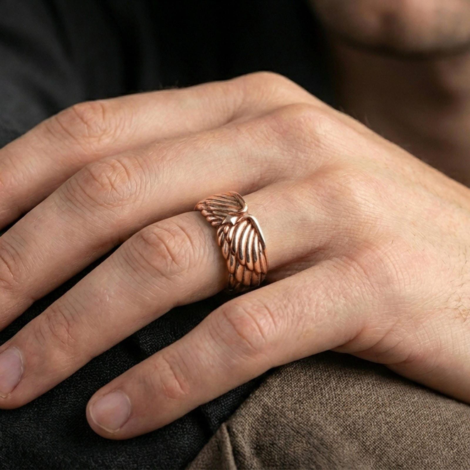 Angel wing sterling silver band ring worn on a finger, rose gold plated finish with elegant warm tones and detailed feather contours.