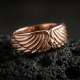 Load image into Gallery viewer, Angel wing sterling silver band ring on black volcanic stone, shown in a rose gold plated finish with a soft warm glow that enhances the layered feather details.
