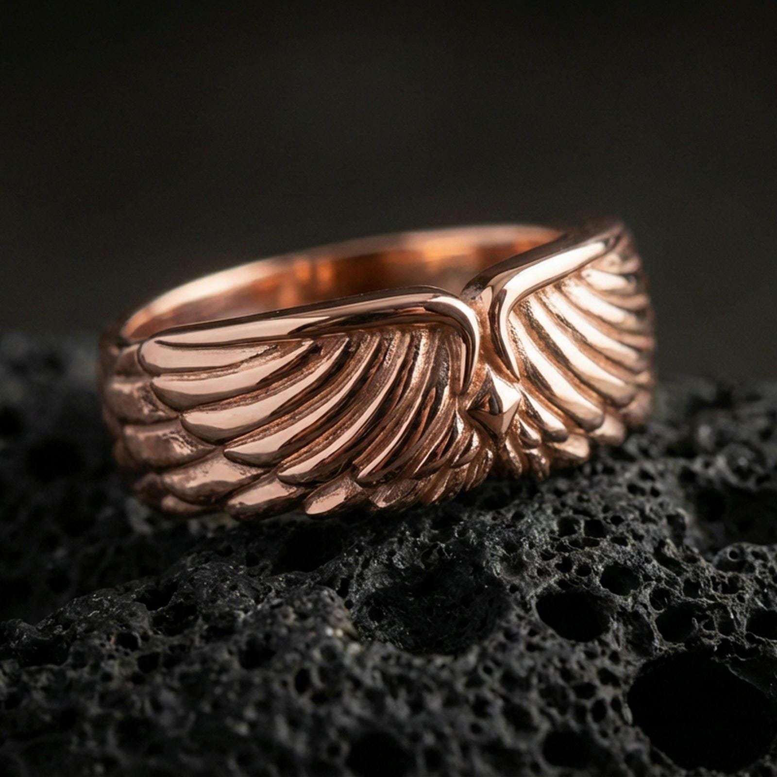 Angel wing sterling silver band ring on black volcanic stone, shown in a rose gold plated finish with a soft warm glow that enhances the layered feather details.