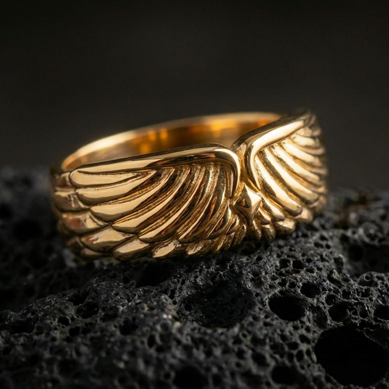Angel wing sterling silver band ring on black volcanic stone, shown in a gold plated finish with warm reflections emphasizing the sculpted wing texture.