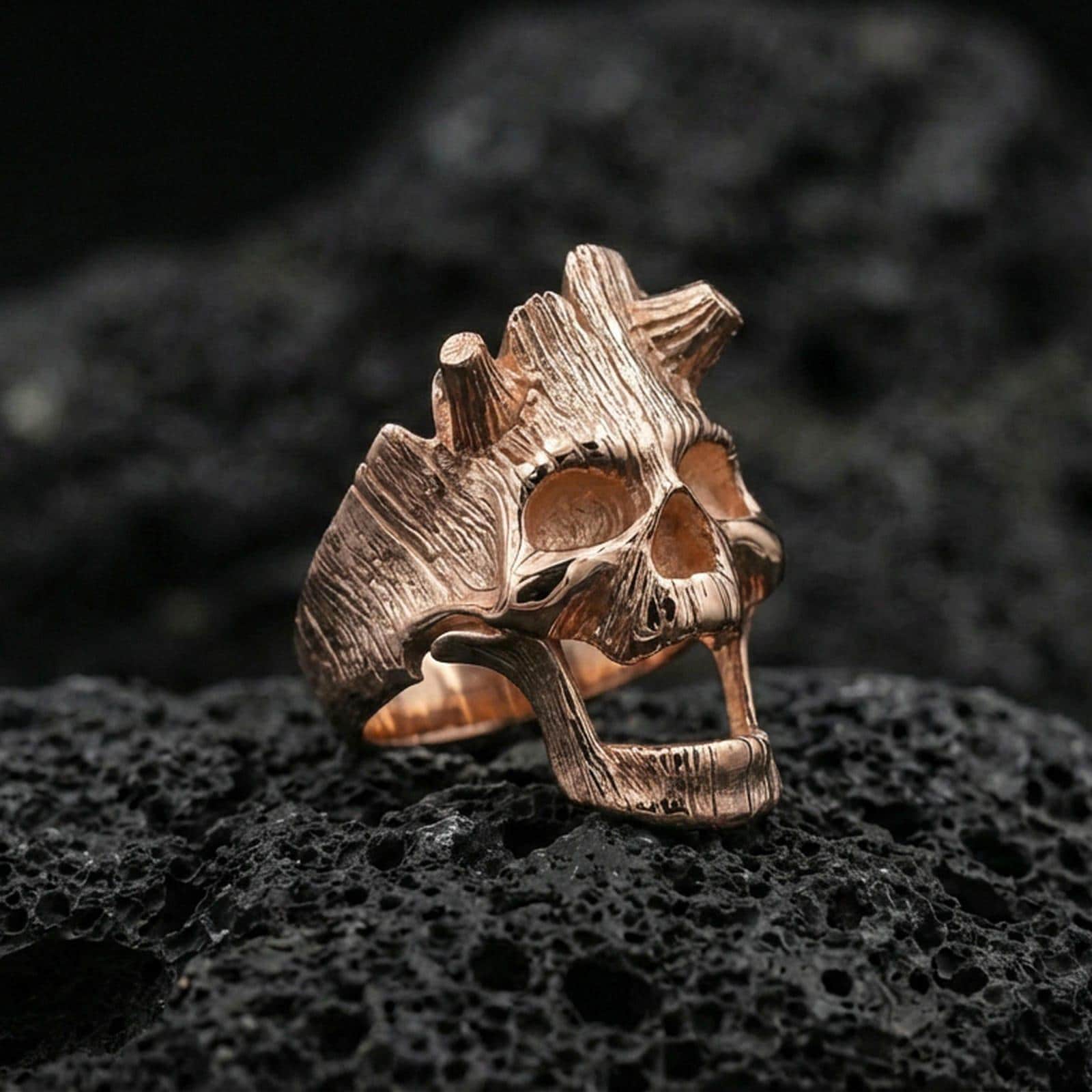 Rose gold plated open skull ring on textured volcanic rock, luxury close-up capturing warm tone, hollow eyes, and sculpted grain lines