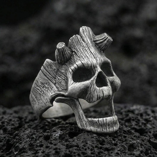 Oxidized sterling silver openwork skull ring on black volcanic rock, macro close-up showing deep patina and woodgrain-style texture lines