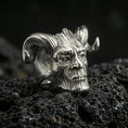 Load image into Gallery viewer, Polished silver horned skull statement ring on porous volcanic stone, close-up highlighting crisp grooves, smooth shine and sculpted face relief
