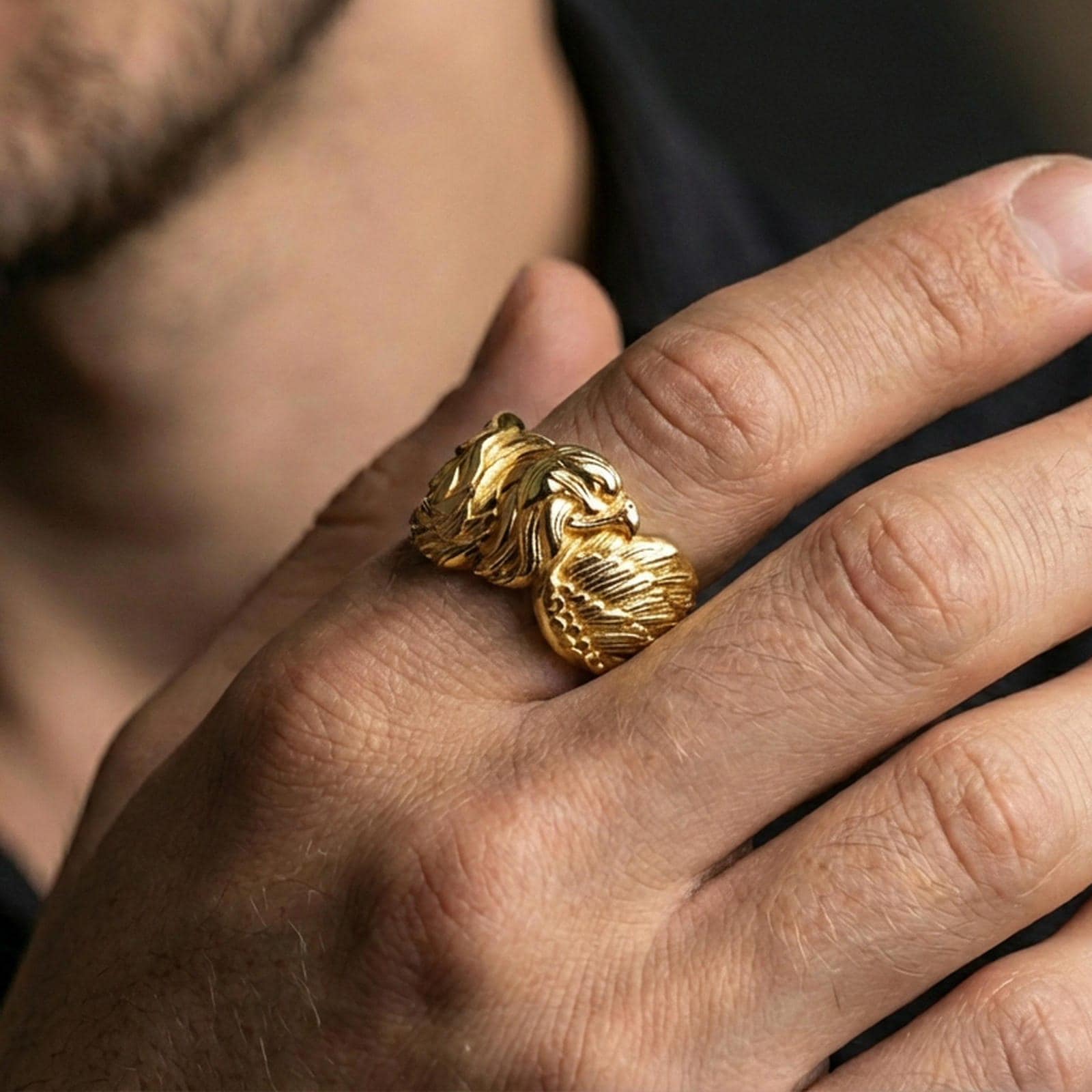 Eagle head and wing sterling silver ring worn on a finger, gold plated finish creating a strong statement look with sharp sculpted edges.