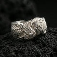 Load image into Gallery viewer, Eagle head and wing sterling silver ring on black volcanic stone, shown in polished silver with bright highlights across the wings and beak contours.
