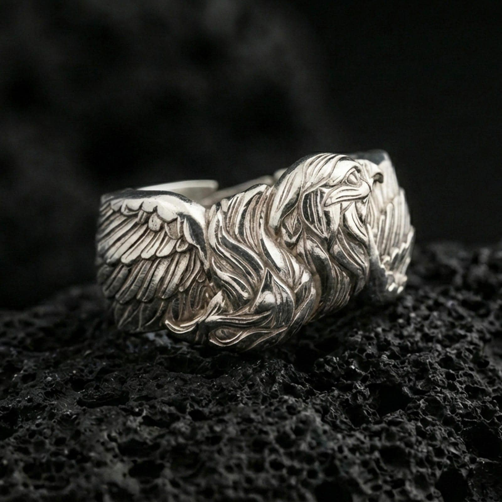 Eagle head and wing sterling silver ring on black volcanic stone, shown in polished silver with bright highlights across the wings and beak contours.