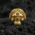 Load image into Gallery viewer, Gold plated laurel crown skull ring on volcanic rock, premium macro photo emphasizing high-contrast leaf engraving, smooth skull dome and shadowed eye sockets
