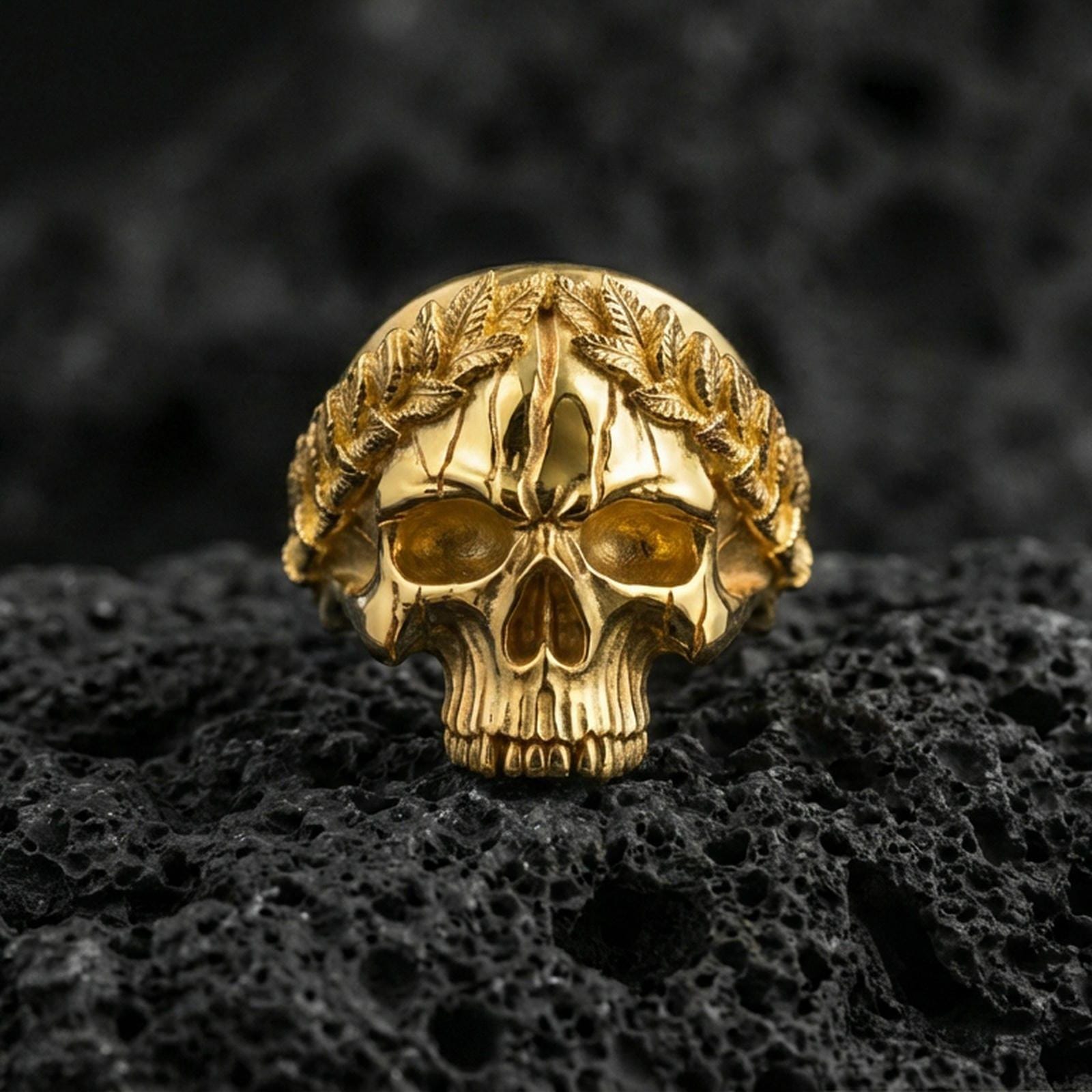 Gold plated laurel crown skull ring on volcanic rock, premium macro photo emphasizing high-contrast leaf engraving, smooth skull dome and shadowed eye sockets