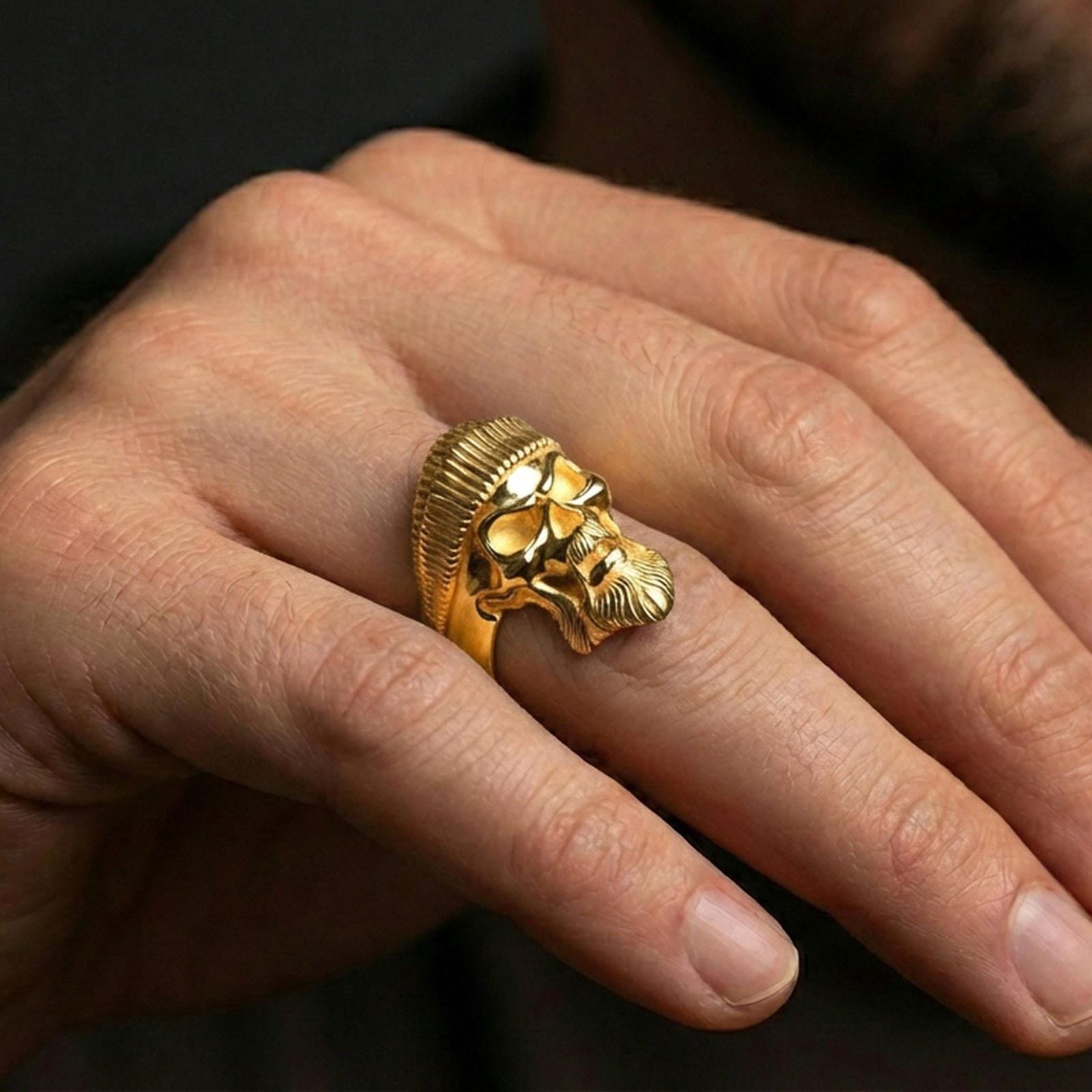Gold plated beret skull ring worn on a finger, lifestyle photo emphasizing bright plating tone, sculpted beard volume and tough gothic character style