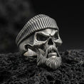 Load image into Gallery viewer, Oxidized sterling silver skull ring with ribbed beret and sculpted beard on black volcanic rock, macro close-up showing deep shadows and rugged biker detailing

