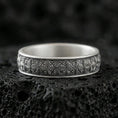 Load image into Gallery viewer, Oxidized sterling silver wedding band on dark volcanic rock, engraved starburst floral texture, premium macro product shot.
