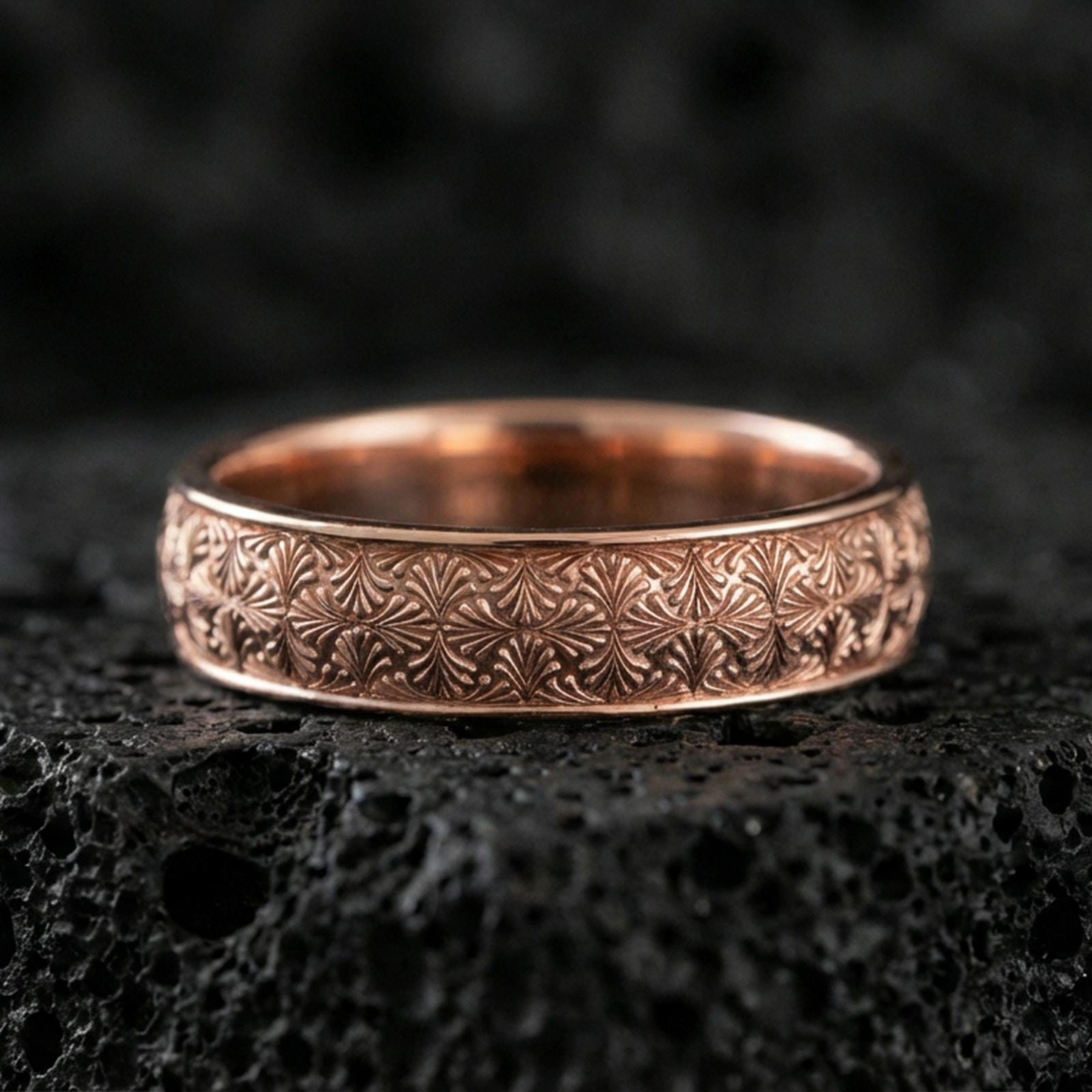 Rose gold plated sterling silver band on volcanic stone, detailed starburst floral engraving, clean minimal high-end close-up.