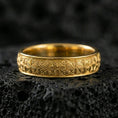 Load image into Gallery viewer, Gold plated textured wedding band on volcanic rock, repeating starburst floral pattern, luxury jewelry product photography.
