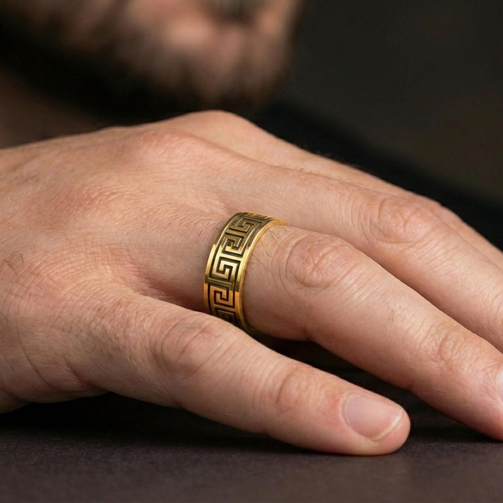Gold plated Greek key pattern band worn on finger, classic meander motif, premium lifestyle jewelry photo.