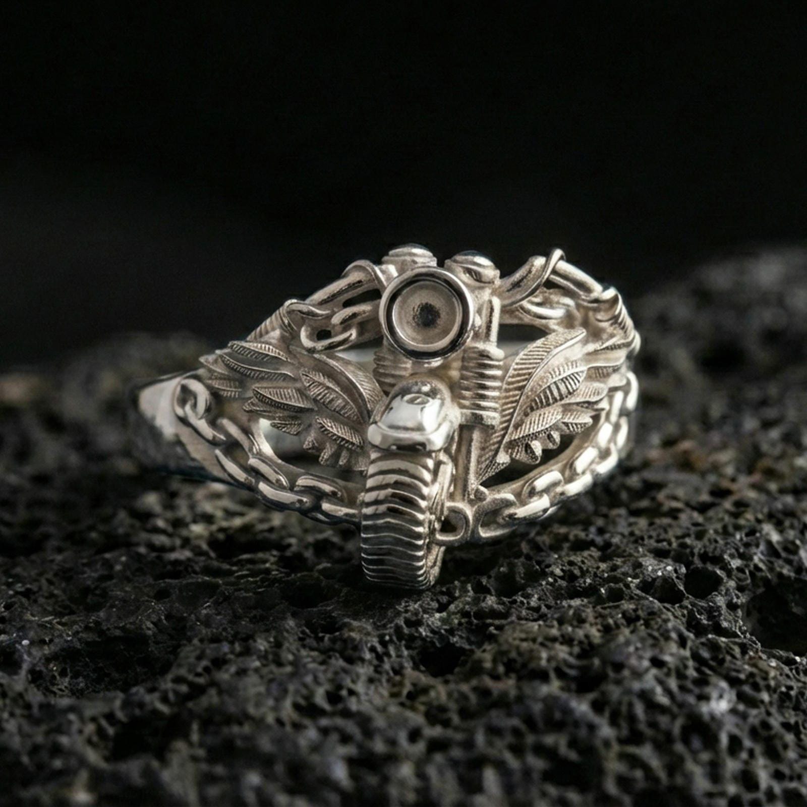 Polished silver biker ring with motorcycle and wing details wrapped in chain links on porous volcanic stone, close-up showing clean shine and sharp sculpted lines