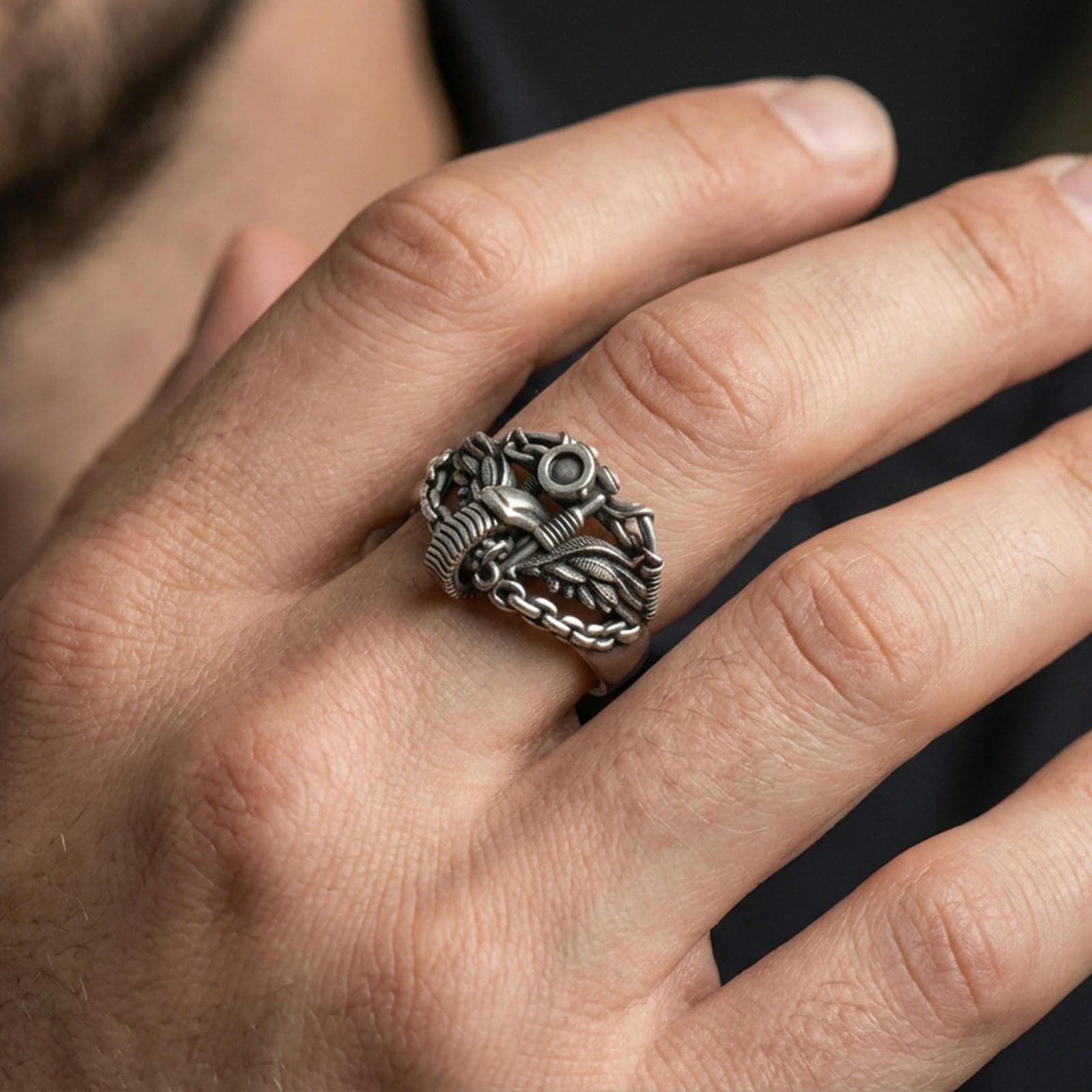 Oxidized motorcycle chain ring worn on a finger, close-up lifestyle shot showing winged bike motif, darkened recesses and rugged biker statement look