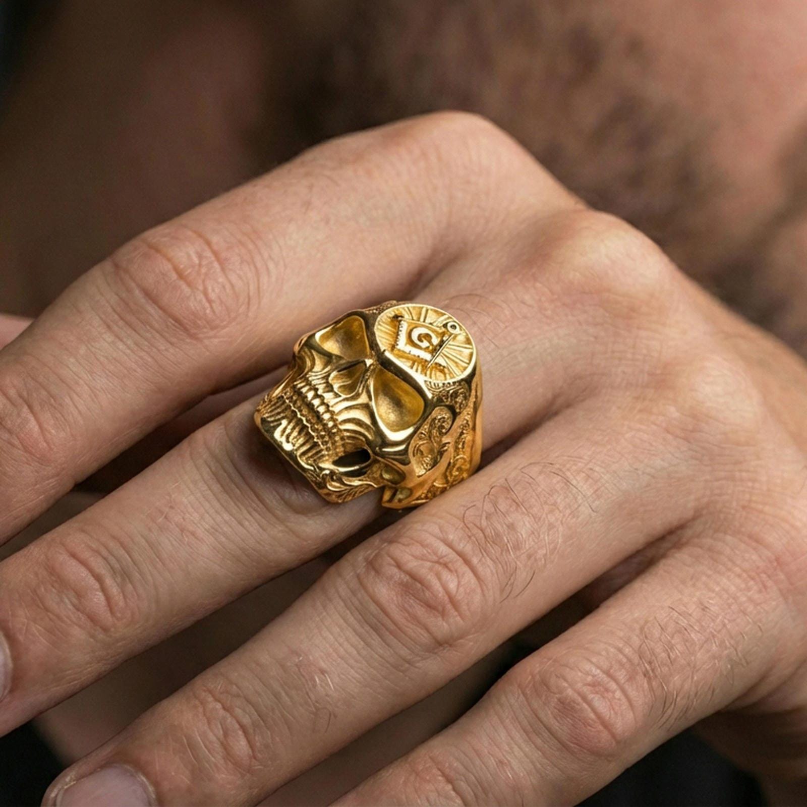 Gold plated skull ring with Masonic square and compass “G” emblem worn on a finger, lifestyle image emphasizing warm tone and bold statement style