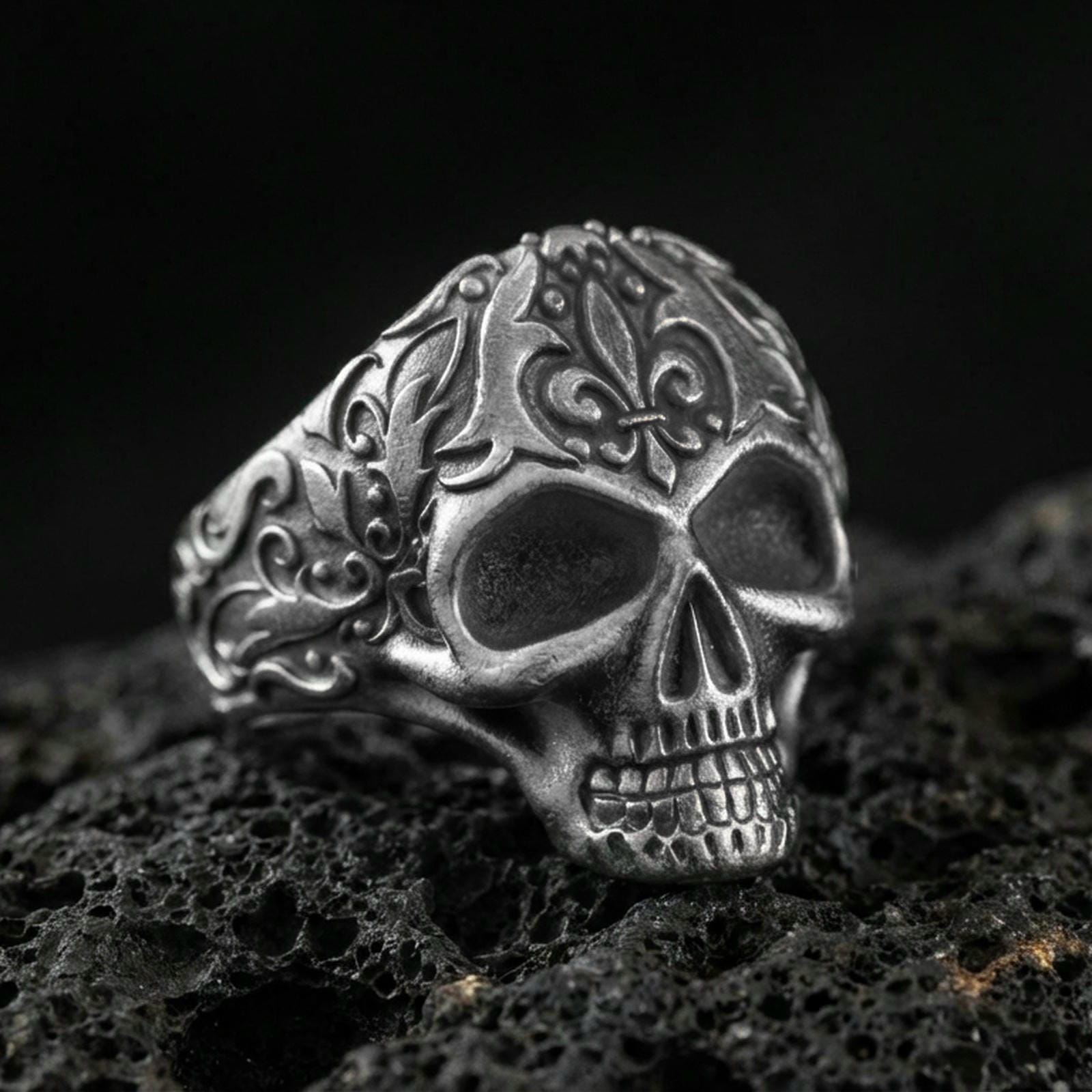 Oxidized sterling silver filigree skull ring with ornate scroll engravings, photographed on black volcanic rock in a dark macro studio setting