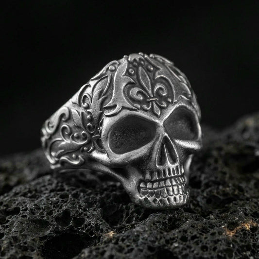 Oxidized sterling silver filigree skull ring with ornate scroll engravings, photographed on black volcanic rock in a dark macro studio setting