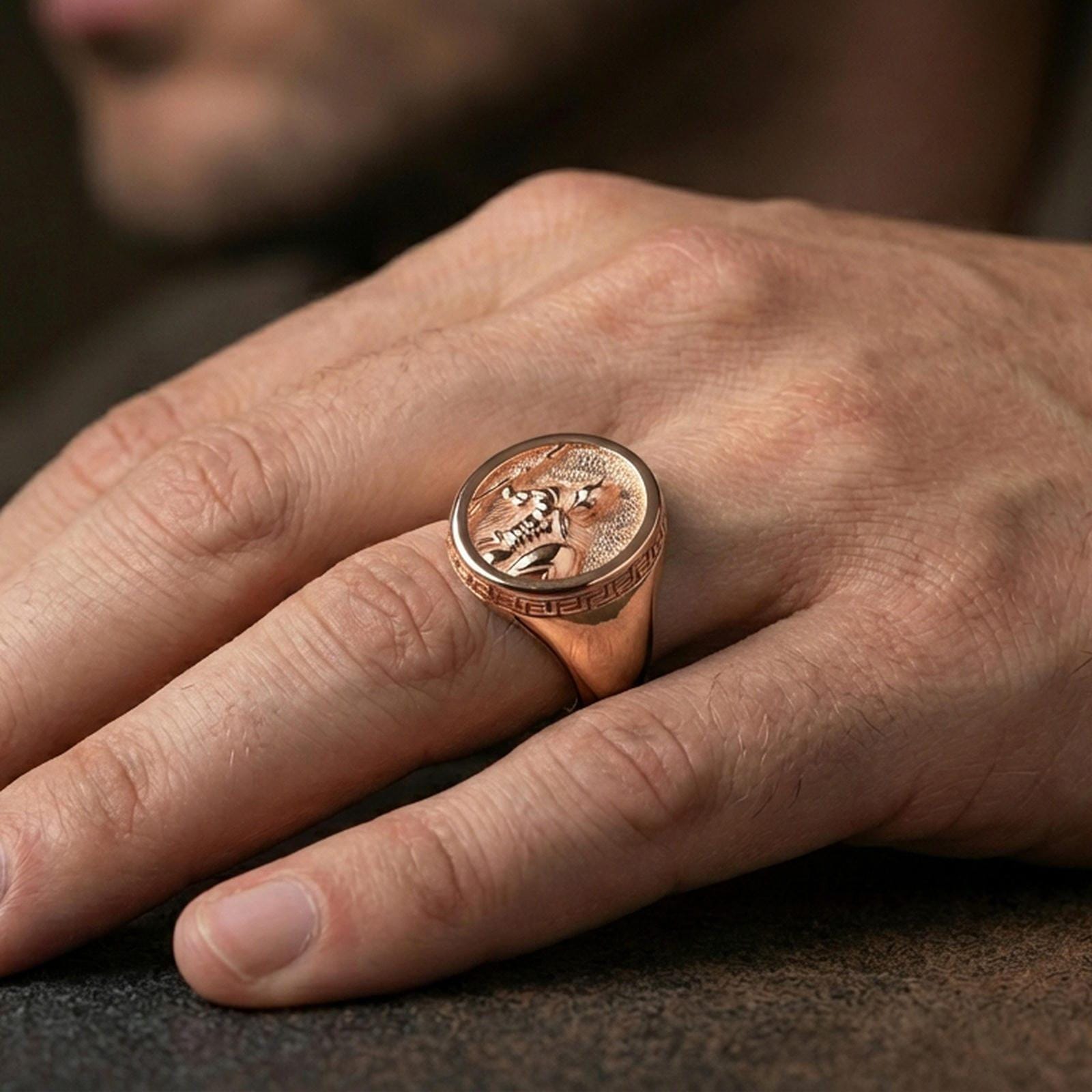 Rose gold plated Greek warrior signet ring worn on a finger, close-up lifestyle shot focusing on the spear-and-shield relief