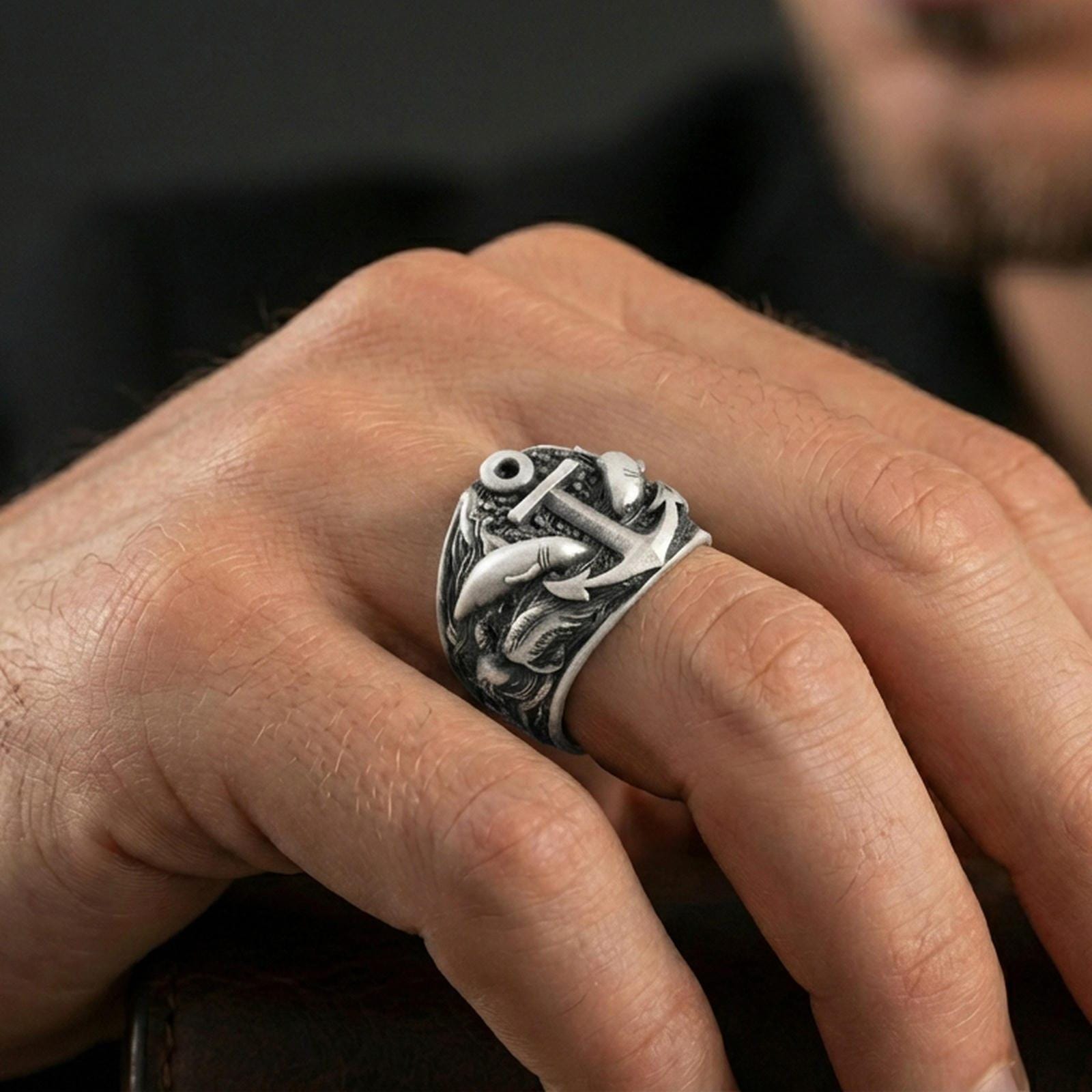 Oxidized anchor and shark ring worn on a finger, close-up lifestyle shot highlighting deep relief and nautical statement style