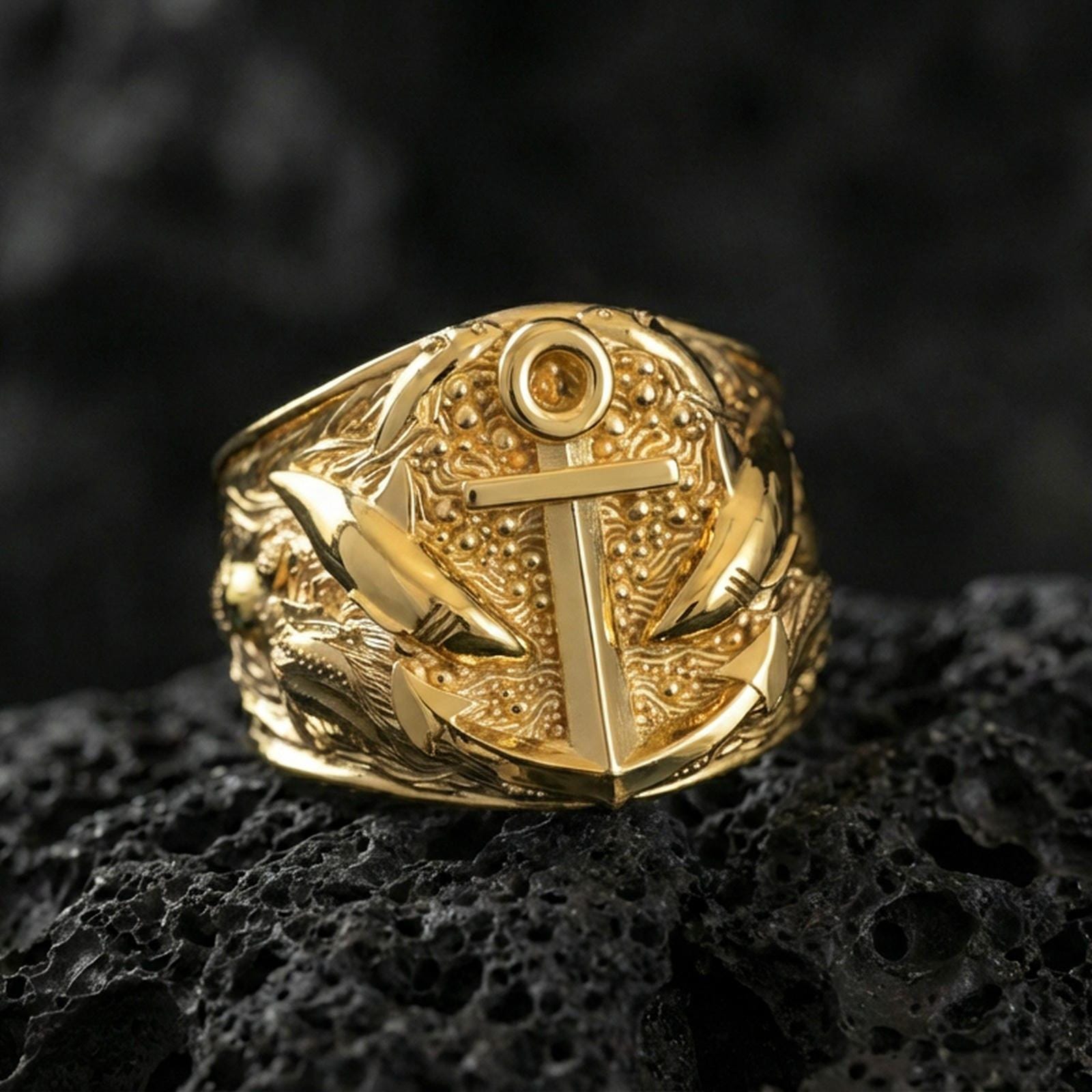 Gold plated anchor statement ring with shark accents and marine-inspired detailing, product-only macro image on black volcanic rock