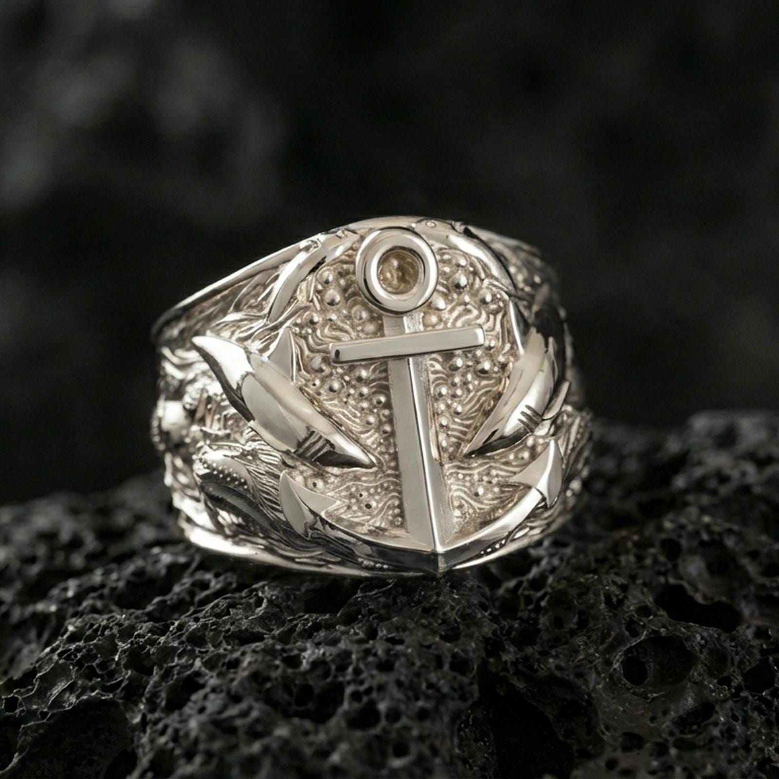 Polished silver nautical anchor ring featuring raised sea-life textures and layered relief, close-up studio shot on porous volcanic stone